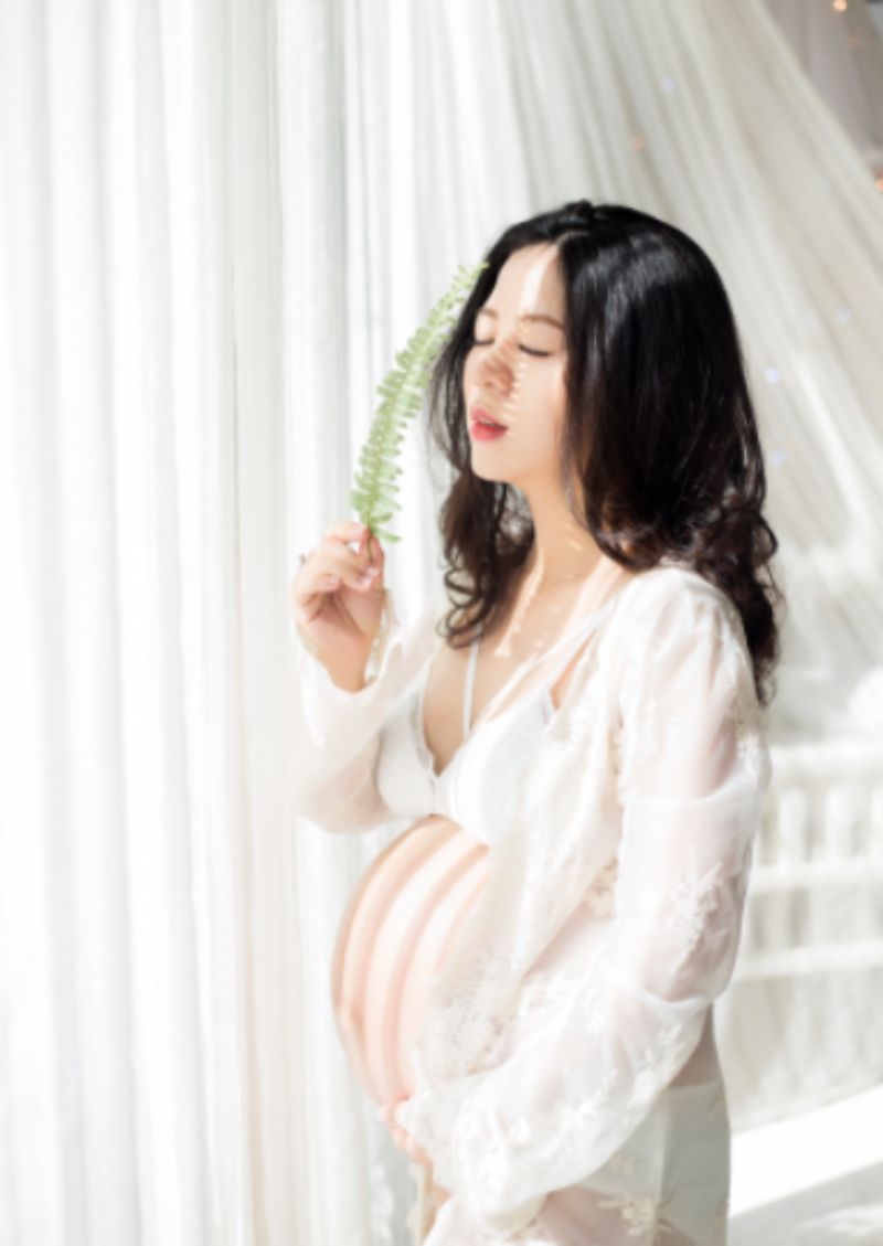 người mẹ đang mang thai đứng cạnh cửa sổ có nắng chiếu
